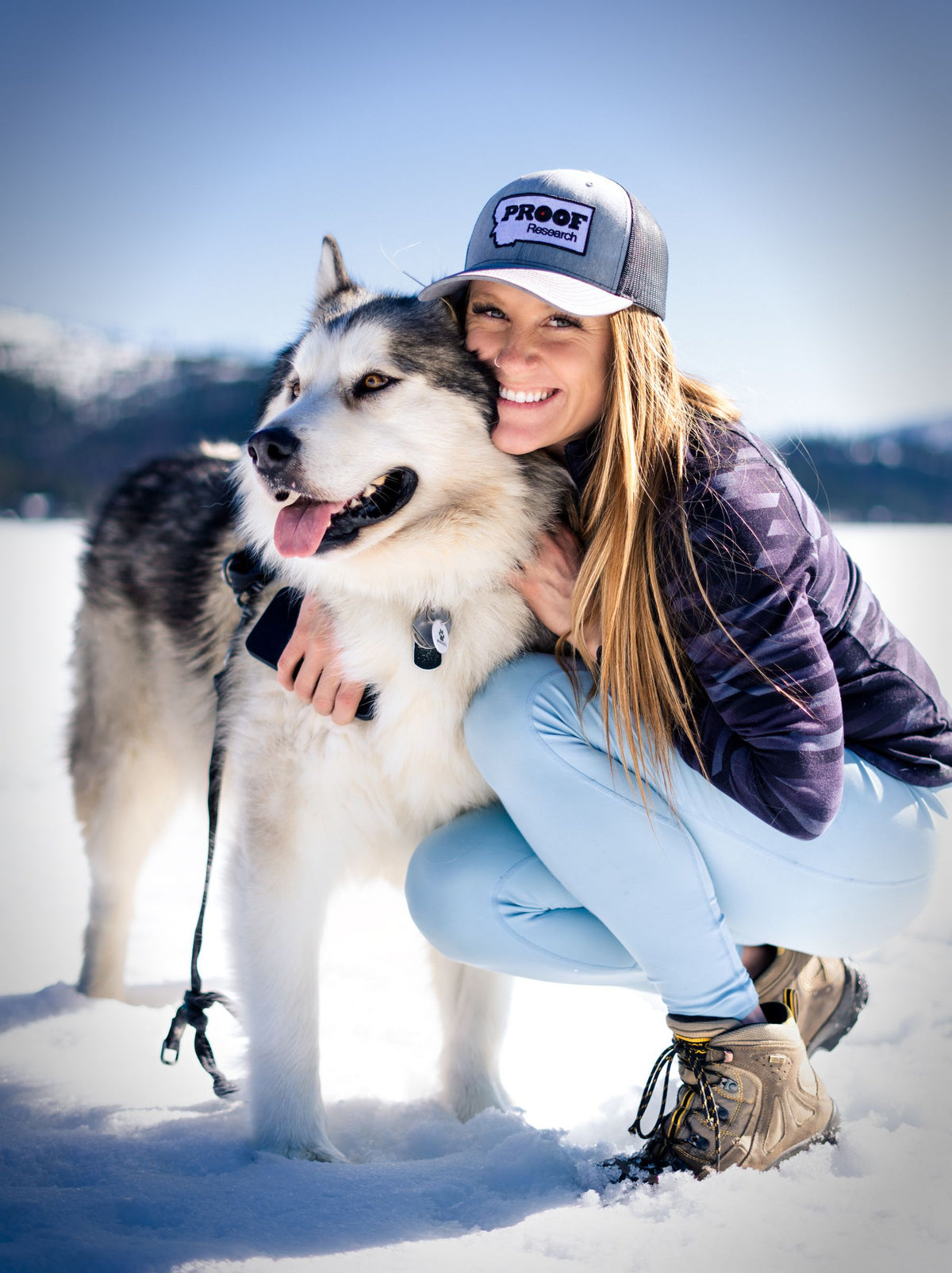 Joven sonriente abrazando a su husky en la nieve