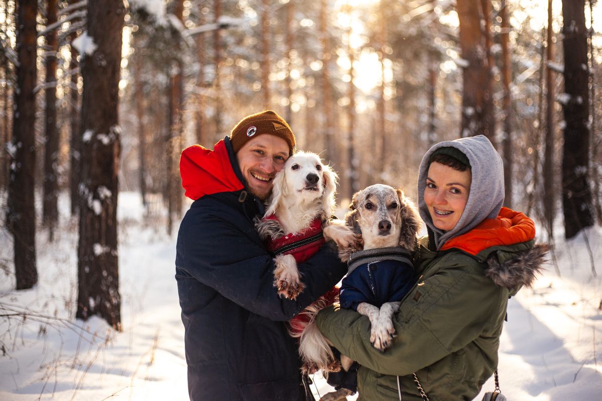 Hombre sonriente con sus dos perros abrigados en un bosque de invierno