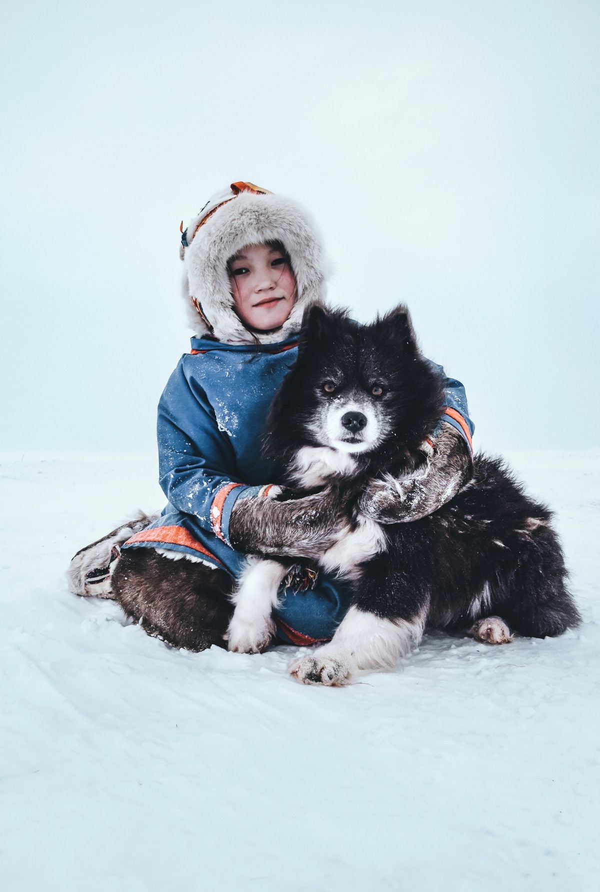 Niña con abrigo de invierno abrazando a su perro en la nieve