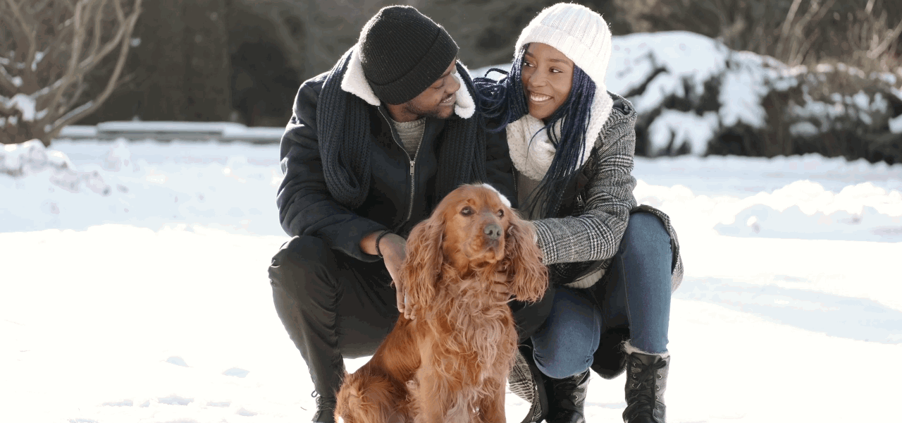 Pareja en la nieve acariciando a su perro